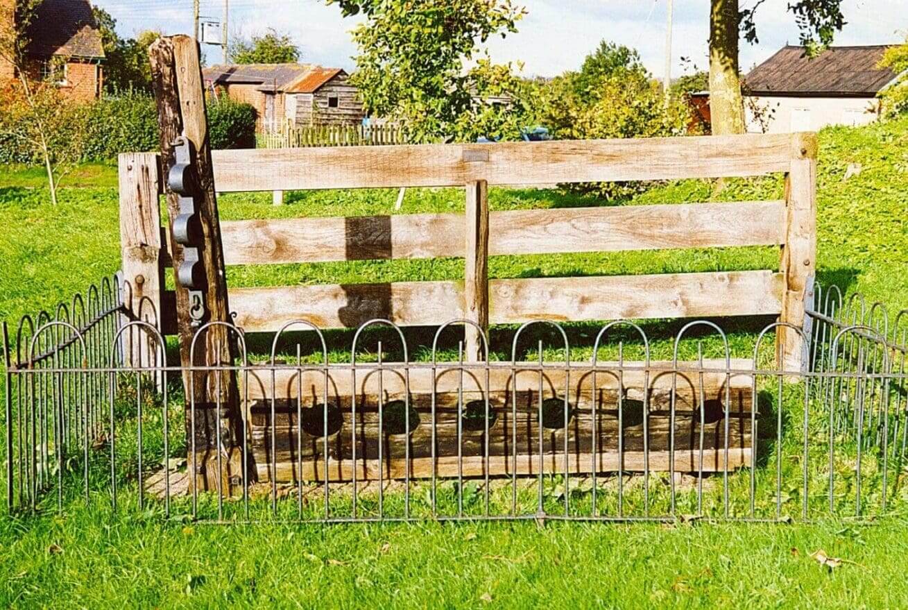 Wooden stocks surrounded by metal fence.